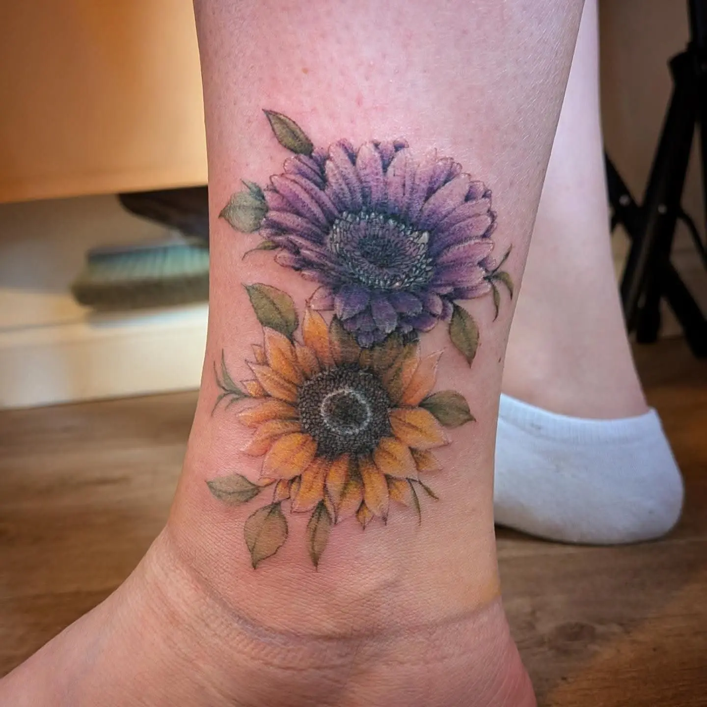 Colour tattoo of a purple gerbera and a sunflower on an ankle