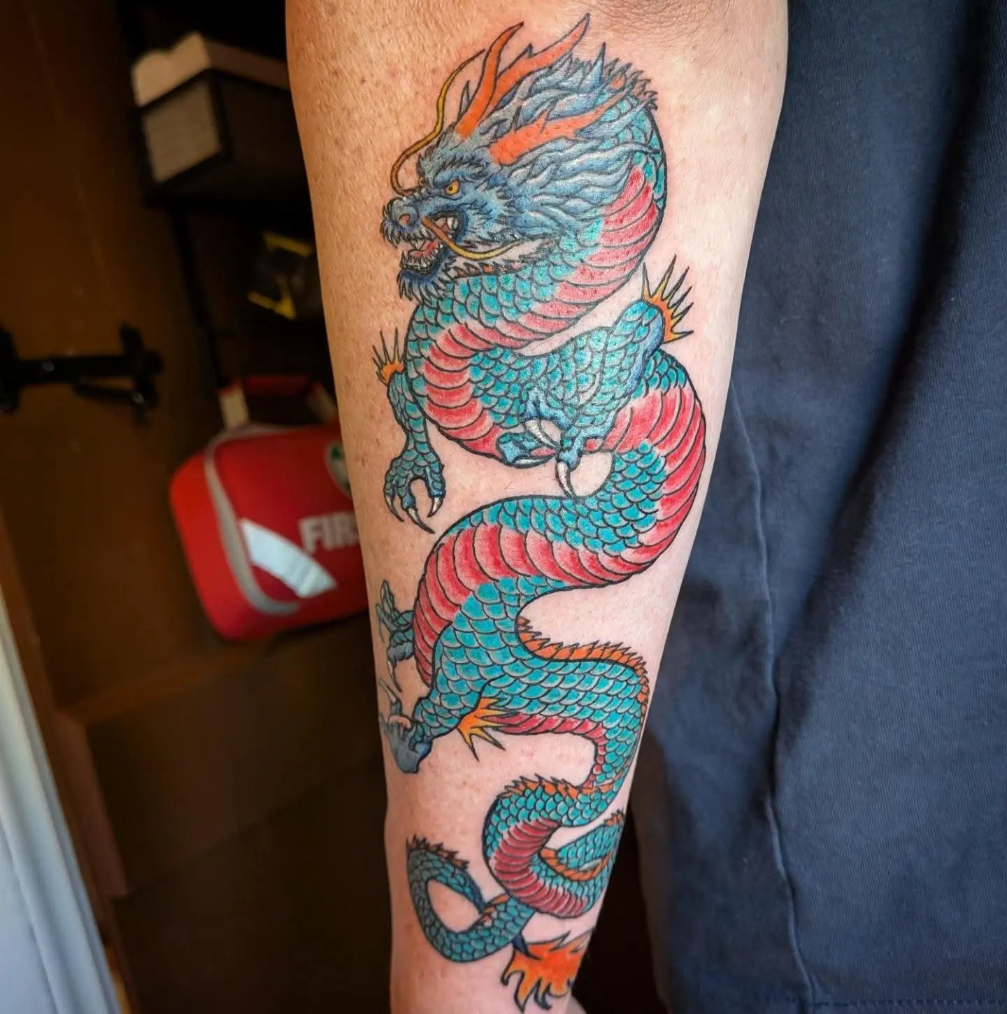 Bold colour tattoo of a blue and red dragon winding down a forearm