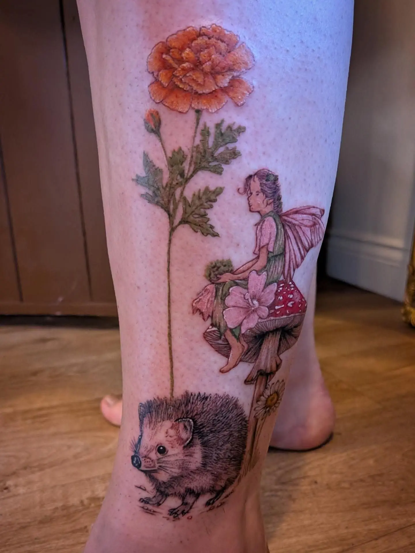 Colour tattoo of a fairy on a toadstool beneath a marigold, with a hedgehog