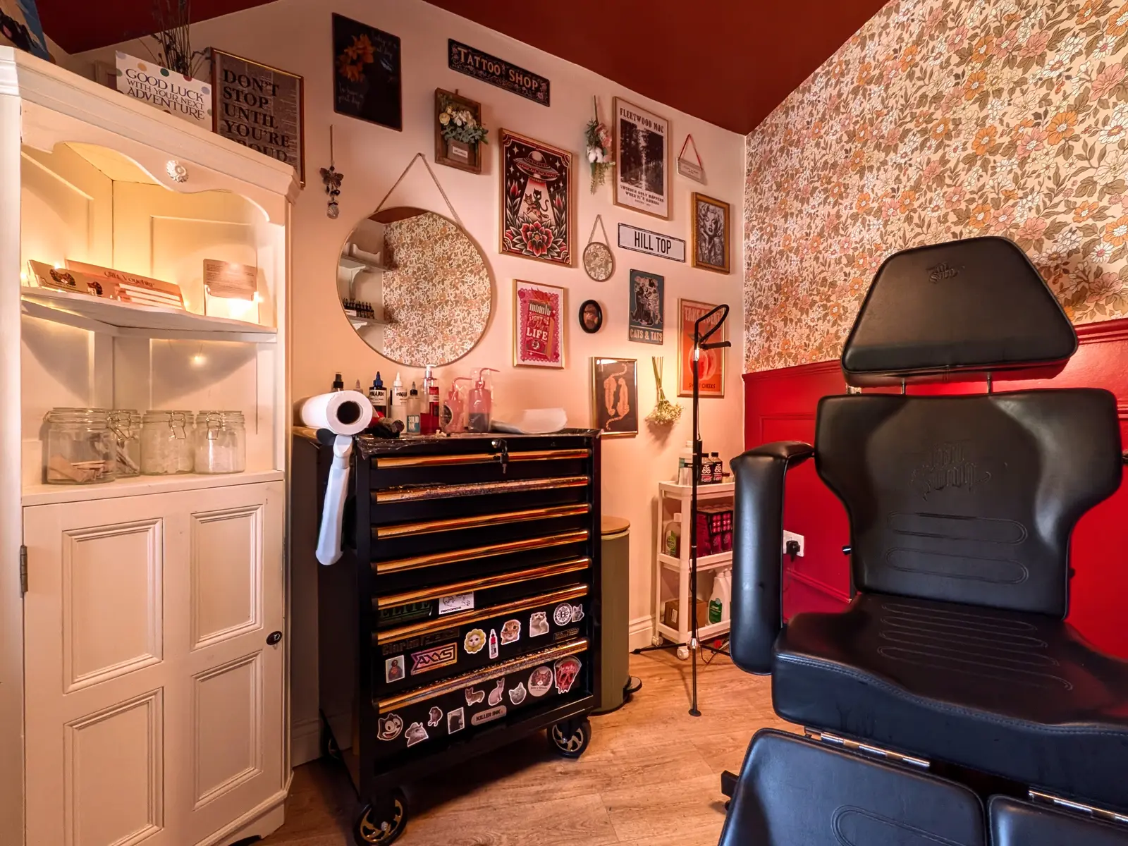 Inside the Berry & Whiskers studio — tattoo chair against red panelling, retro floral wallpaper and a gallery wall of prints